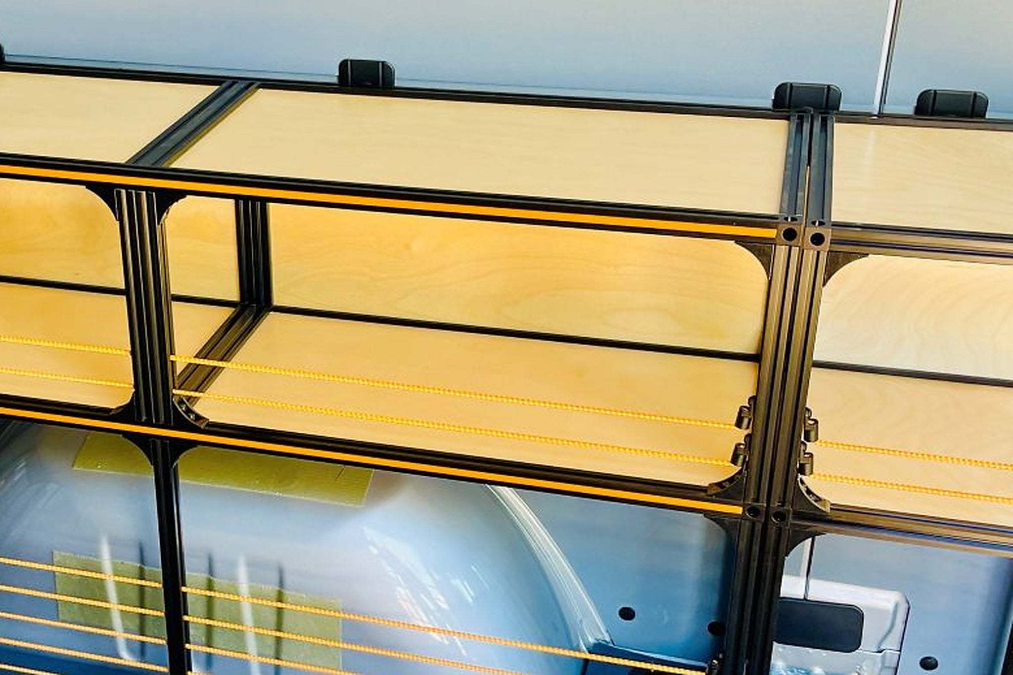 Close view of a bolted shelf run along the interior side wall of a work van, stock retained behind straps