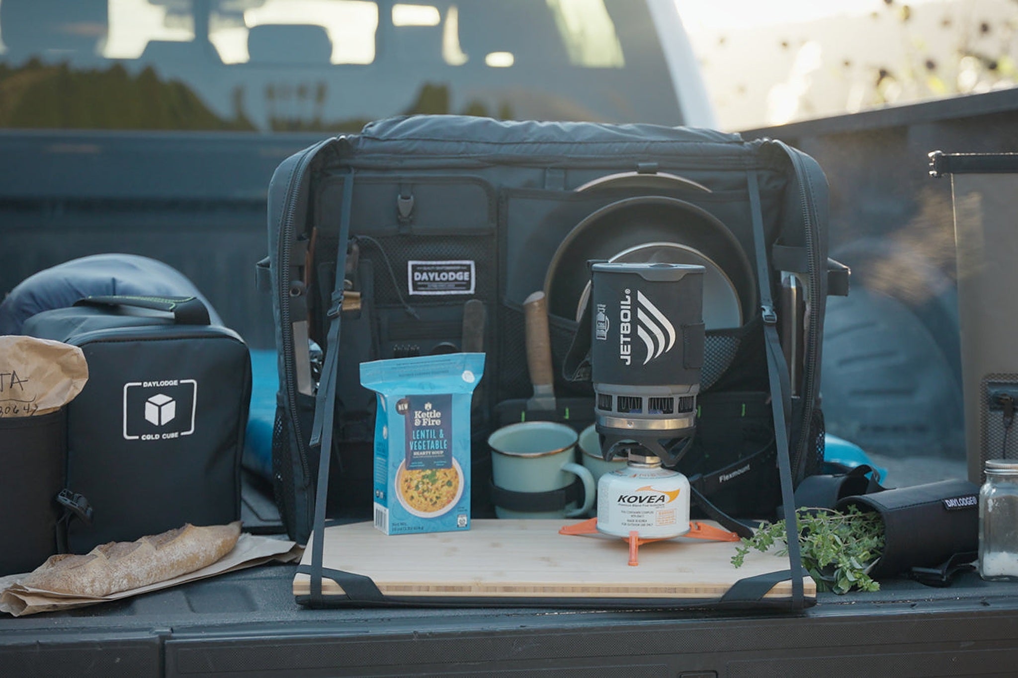 Close view of a loaded gear bay in a van with cases and a cook set laid out on a bamboo surface