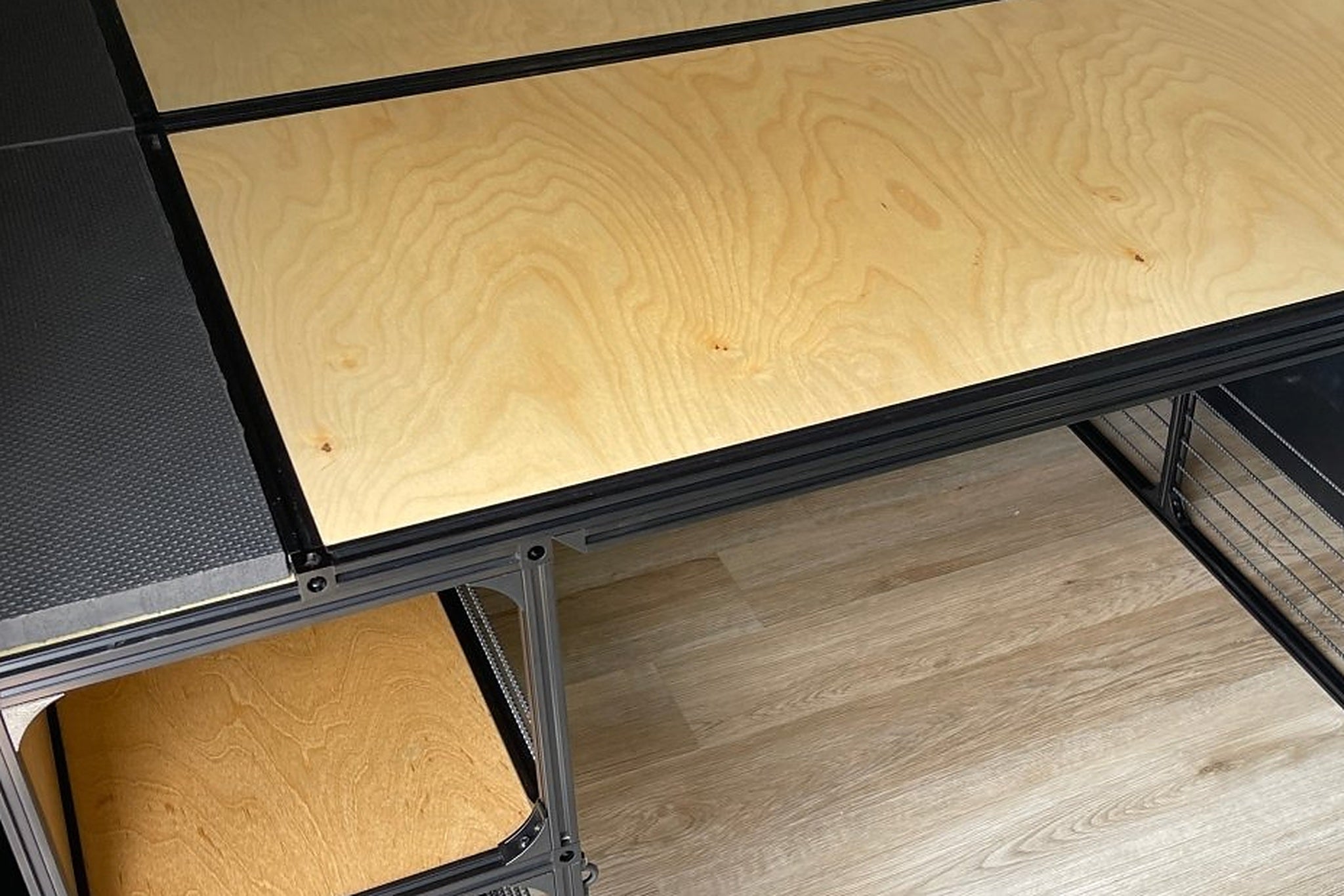 Close view of a black square-tube shelf frame carrying a factory-finished birch shelf