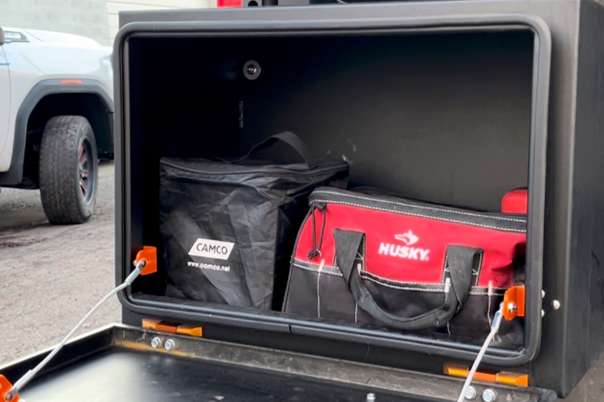 Close view inside an open exterior tool box on a van, tool bags stowed on the shelf