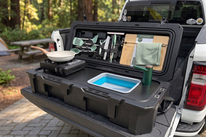 A hard case camp kitchen opened out on its legs beside a van