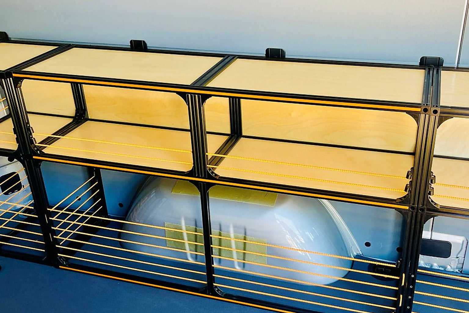 Black steel tube and birch plywood shelving fitted over the wheel arch inside a high-roof cargo van
