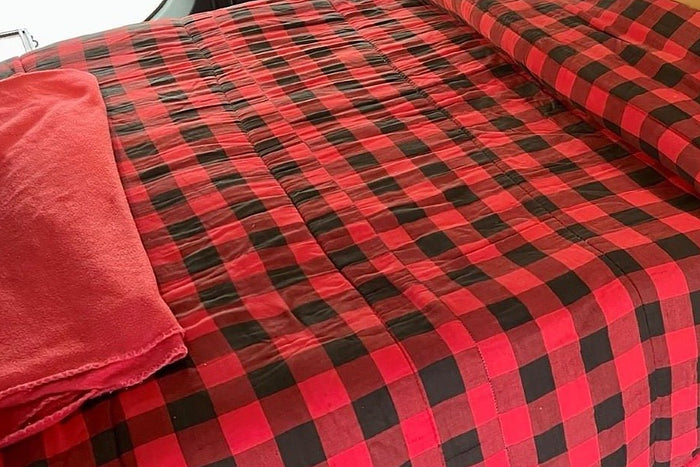 Plaid bedding made up on a camper van bed platform