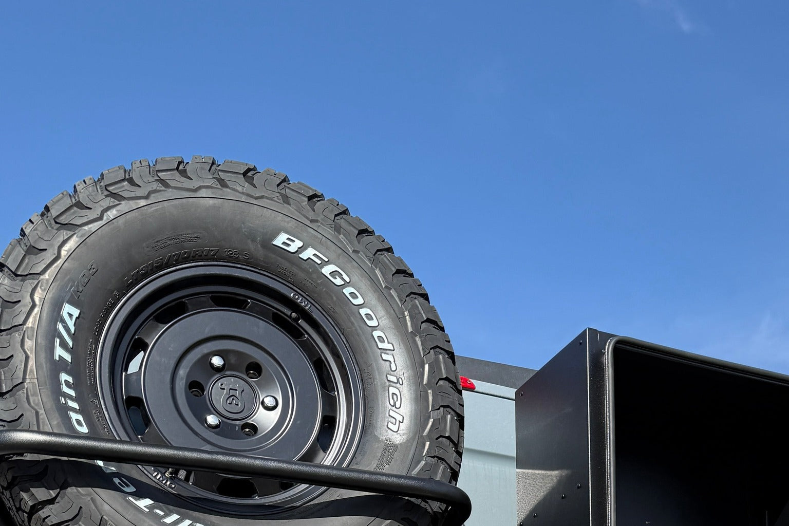 Full-size spare tire on a van door carrier against blue sky