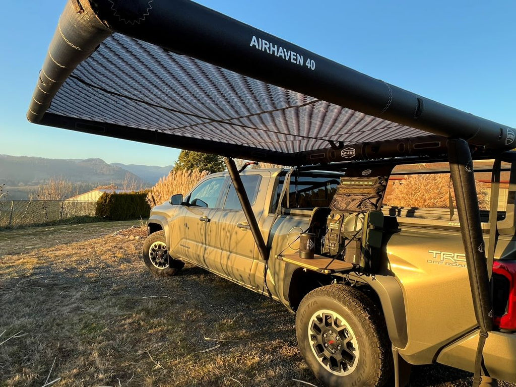 DAYLODGE AirHaven 40 vehicle shelter set up in carbon camo beside a Toyota Tacoma at camp