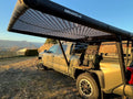 DAYLODGE AirHaven 40 vehicle shelter set up in carbon camo beside a Toyota Tacoma at camp