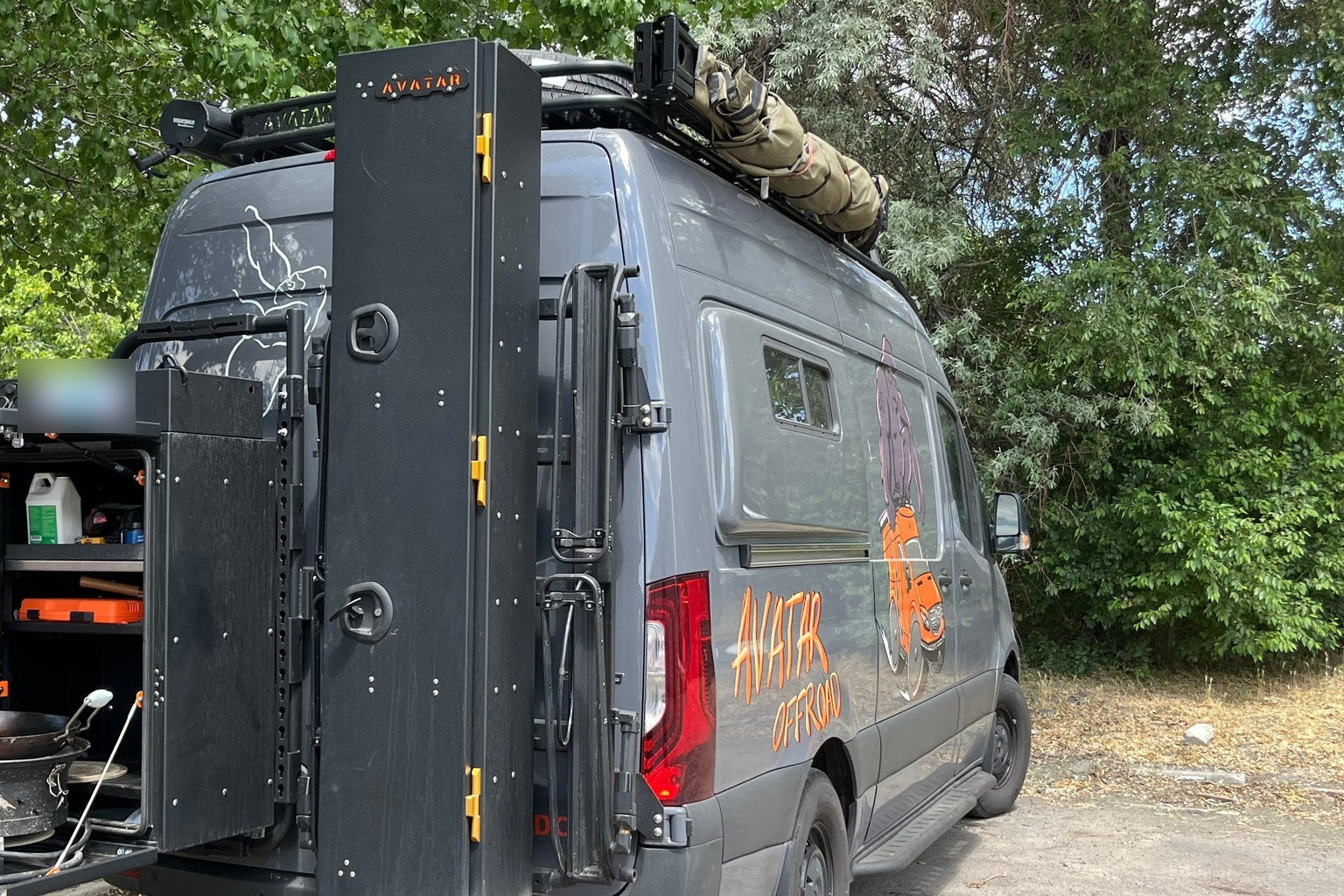 A vehicle awning deployed over a pickup bed at a quiet grassy pull off, set up as a basecamp